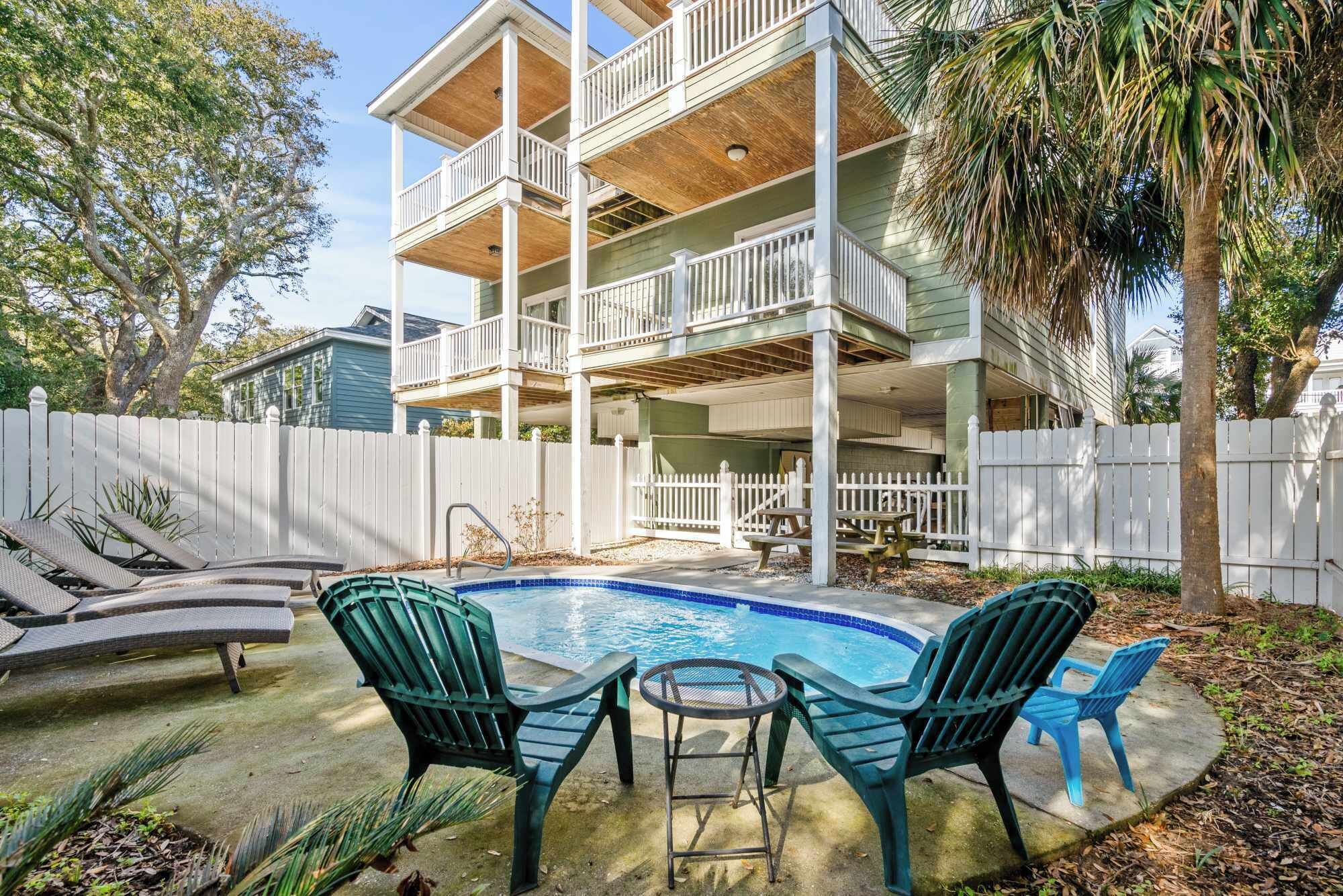 A two-story house with a pool, outdoor furniture, and a white picket fence.