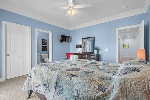 A bedroom with a bed, a ceiling fan, a TV, and a mirror.