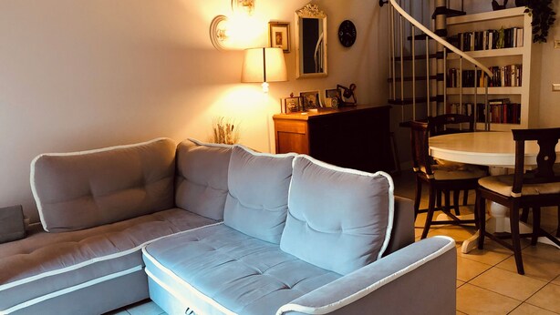 A living room with a grey sectional sofa, a dining table with chairs, a staircase, and a bookshelf. - Zelda's House - 500 meters from the center (Cremona)