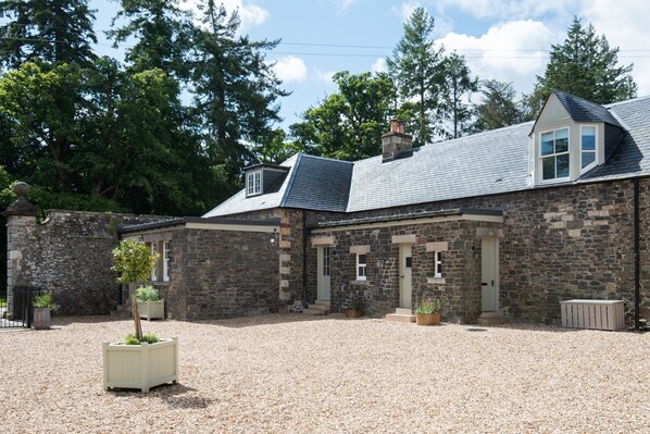 A stone building with a gravel driveway and a small garden area with potted plants.