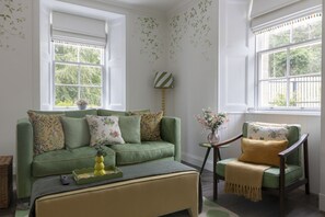 A room with a green sofa, a small side table, and a chair with a throw blanket.
