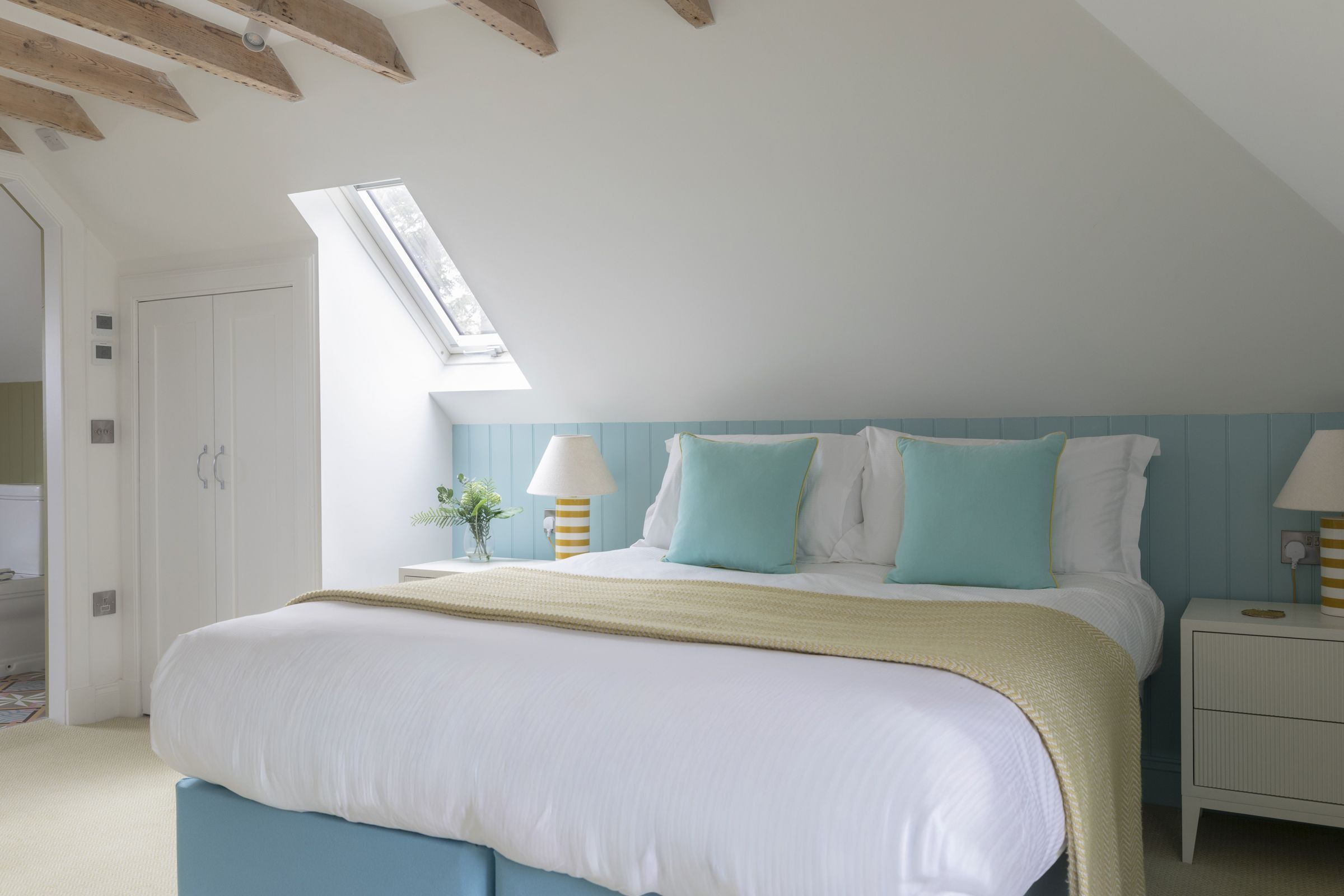 A bedroom with a bed, bedside tables, a lamp, a window, and a skylight.