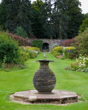 A stone urn in a garden with a pathway leading to a stone archway.