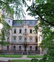 A historic building with a symmetrical facade, multiple windows, and a central entrance with steps leading up to it.