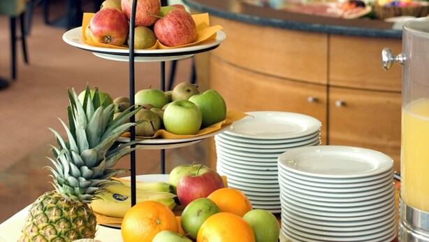 Montaje de bufé con frutas y platos variados, que incluye un frutero de tres niveles, tazones de frutas y platos apilados.