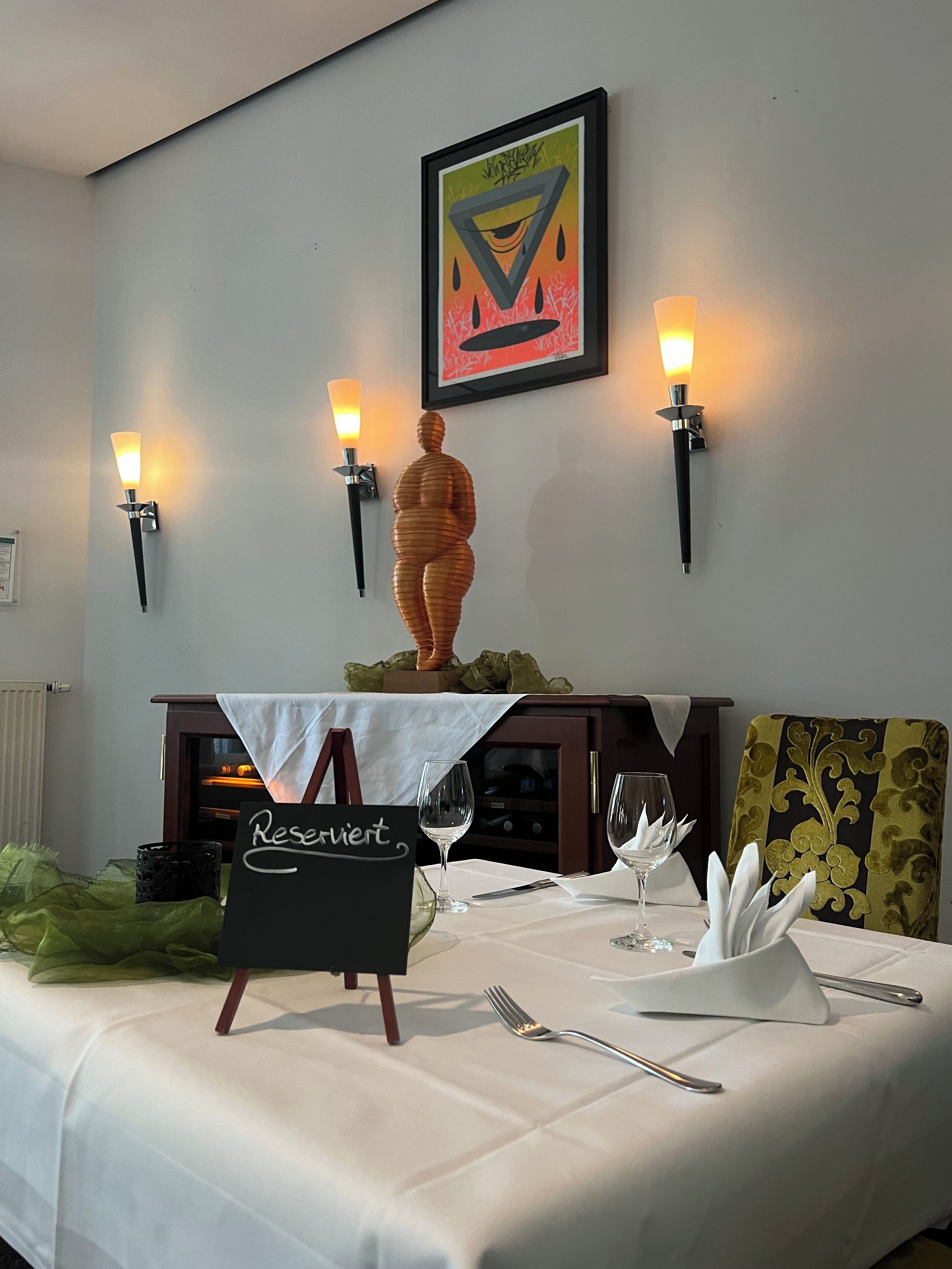 Une table à manger dressée, avec une pancarte indiquant « Réservé », des verres à vin et une sculpture décorative.
