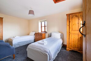 Une chambre avec deux lits simples, une armoire en bois, une petite fenêtre et un luminaire au plafond.