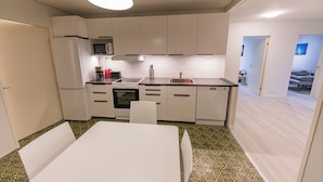 Cocina compacta con armarios blancos, microondas, fregadero y comedor con mesa y sillas.