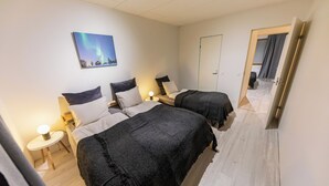 Una habitación de hotel con dos camas, una mesita de noche con lámpara, un cuadro en la pared y una puerta que da a otra habitación.