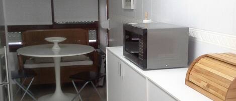 Una cocina compacta con microondas, un reloj y una tabla de cortar de madera sobre la encimera.