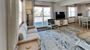 A spacious living room with a sofa, a television, and a dining area. - Blue Lagoon | Water Views + Walkable Beach Access (Topsail Beach)