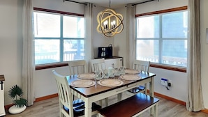 A dining area with a wooden table, white chairs, and woven placemats. - Blue Lagoon | Water Views + Walkable Beach Access (Topsail Beach)