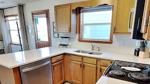 A modern kitchen with wooden cabinets, a stainless steel dishwasher, a double sink, and a black stove. - Blue Lagoon | Water Views + Walkable Beach Access (Topsail Beach)