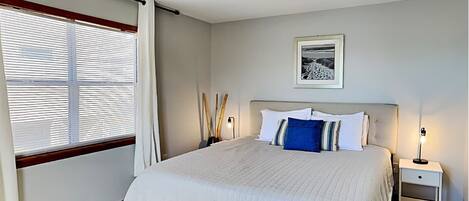 A bedroom with a bed, bedside tables, a ceiling fan, a window with blinds, and a framed picture on the wall.