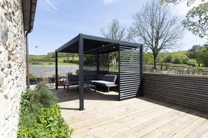 A wooden deck with a covered seating area, a stone wall, and a view of the countryside.