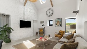 A living room with a sofa, a coffee table, a clock, a TV, and a window with a view. - Stylish barn conversion, sleeps 5, with hot tub (Carmarthen)