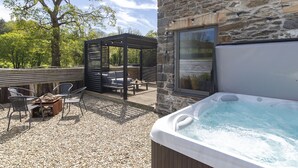 A stone building with a hot tub, outdoor seating, and a pergola. - Stylish barn conversion, sleeps 5, with hot tub (Carmarthen)
