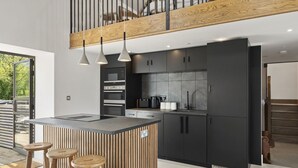 A modern kitchen with a central island, wooden stools, and a view of the outdoors. - Stylish barn conversion, sleeps 5, with hot tub (Carmarthen)