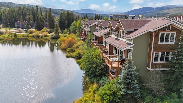 A lakeside resort with wooden decked buildings, a view of the lake, and mountains in the background.