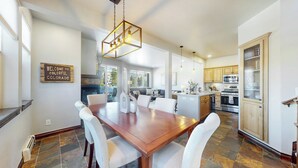 A spacious kitchen with a dining area, featuring a wooden table, white chairs, and a modern chandelier.