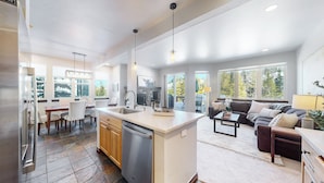 A spacious kitchen with a central island, dining area with chairs, a sofa, and a coffee table.