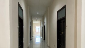 A long, narrow hallway with a shiny tiled floor and white walls. There are doors on both sides of the hallway, and a window at the end.