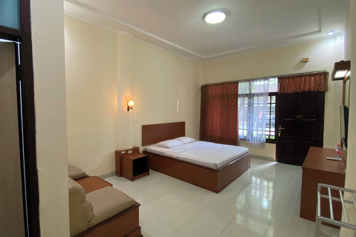 A hotel room with a bed, a nightstand, a desk, a chair, and a wardrobe.