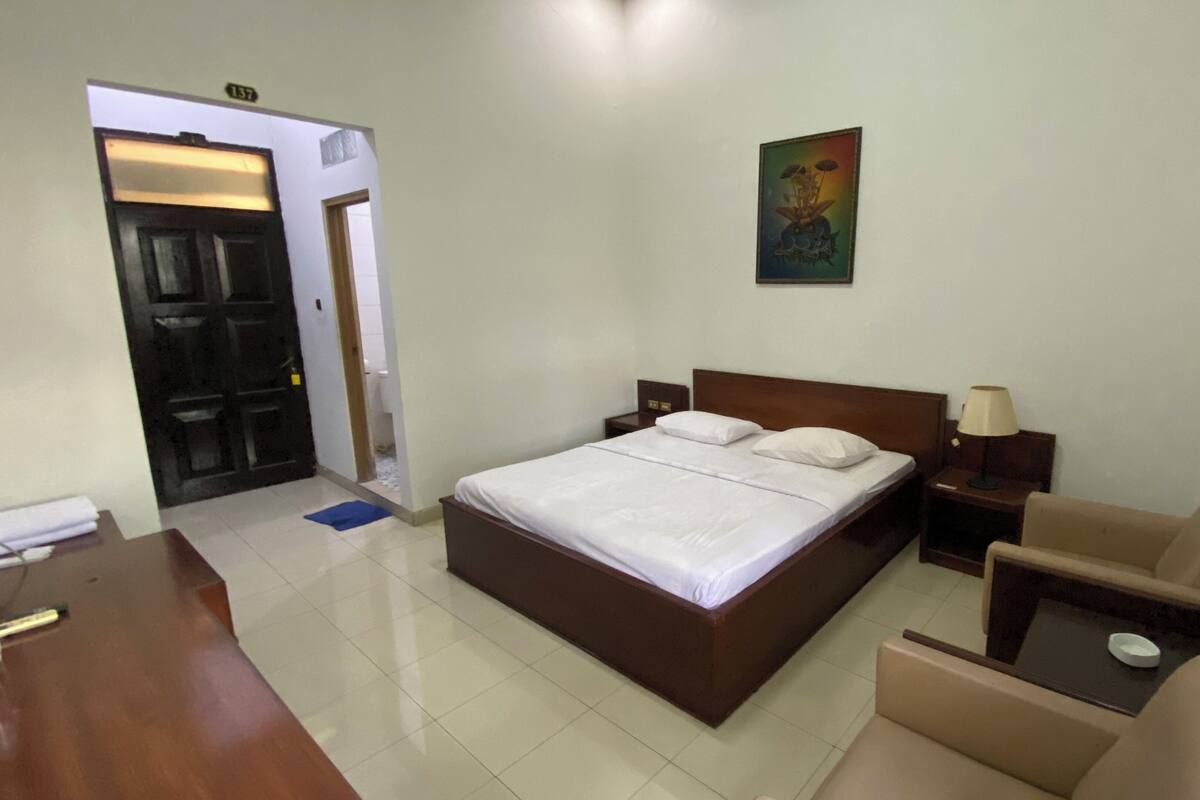 A hotel room with a large bed, a desk, a chair, and a small table.