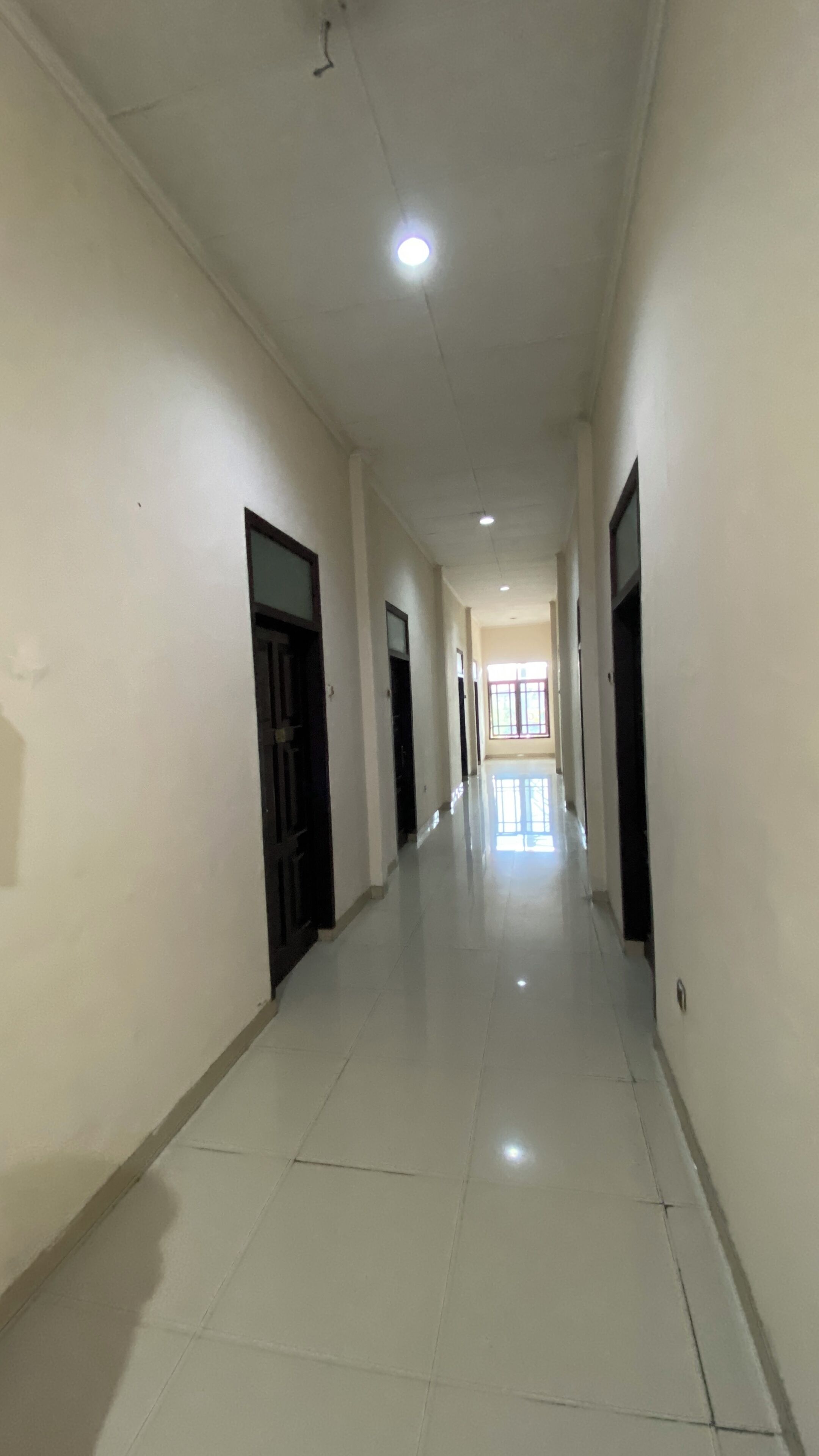A long, narrow hallway with white walls and a shiny tiled floor.