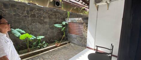 Un muro de piedra con plantas, suelo de baldosas, una silla de madera y una mesa.
