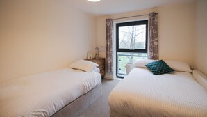 Un dormitorio con dos camas individuales, una mesita de noche con lámpara, una ventana con cortinas y vistas al exterior.