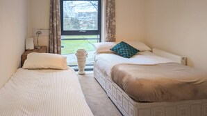 Un dormitorio con dos camas individuales, una mesita de noche con lámpara, un florero y una ventana con cortinas.
