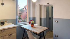 Eine kleine Küche mit Fenster, Tisch mit Vase und Schrank mit Gläsern.