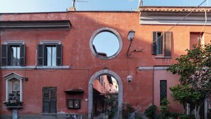 Ein schmaler Gang mit einem Rundfenster und einem Bogen, der zu einem Gebäude mit roter Fassade führt.
