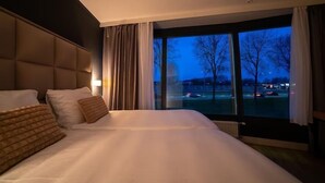 Habitación de hotel con una cama grande, vista a un estacionamiento y una ventana con cortinas.