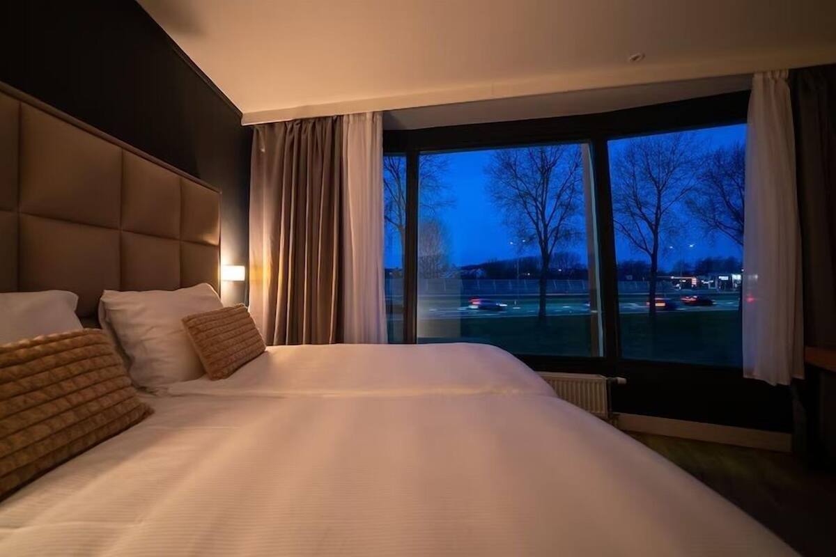 A hotel room with a large bed, a view of a parking lot, and a window with curtains.