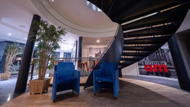 Un interior moderno con techo curvo, sillas azules, una escalera y vistas a la ciudad.