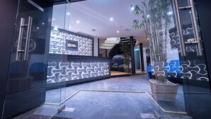 Un área de recepción moderna con entrada de vidrio, un mostrador con un diseño de luz geométrico y una escalera que conduce a un nivel superior.