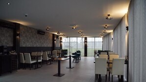 Un espacio interior amplio con varias mesas y sillas de comedor, una zona de bar y grandes ventanales que dejan entrar luz natural.