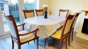 Ein Esszimmer mit einem runden Tisch, sechs Stühlen, einer Blumenvase und einem Fenster.