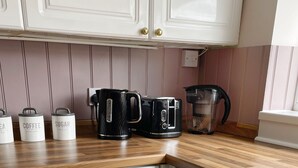 Eine Küche mit weißen Schränken, einer Holz Arbeitsplatte und verschiedenen Geräten, darunter eine Kaffeemaschine und ein Wasserkocher.