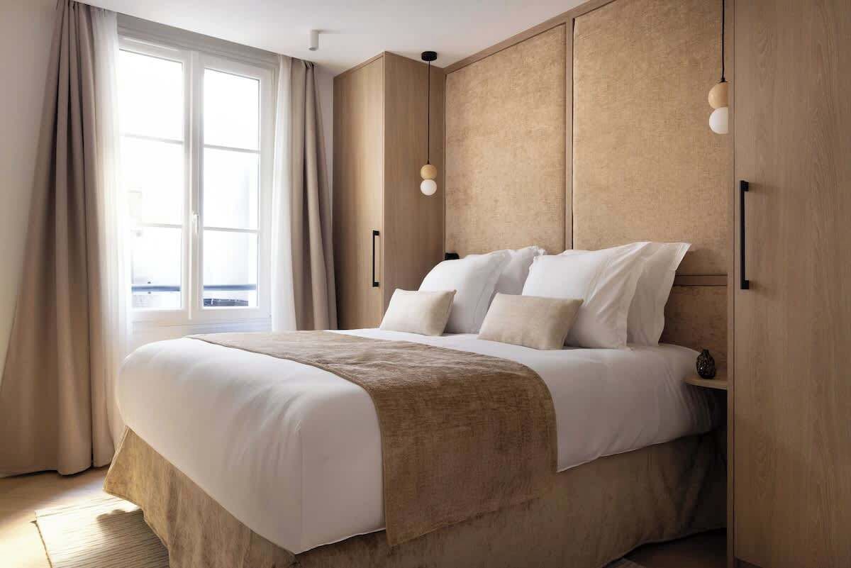 A modern hotel room with a large bed, beige walls, and a window with curtains.
