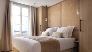 A modern hotel room with a large bed, beige walls, and a window with curtains.