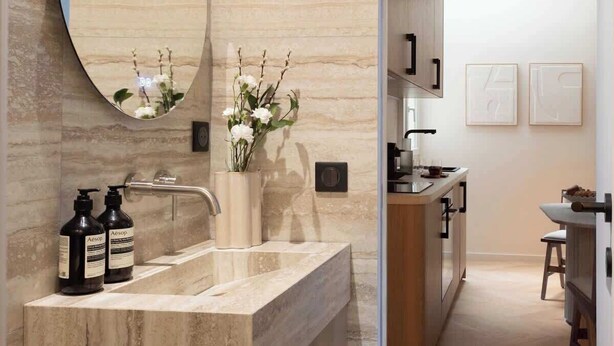 A modern bathroom with a marble vanity, a large mirror, and a vase with flowers.