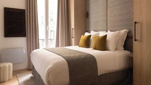 A modern hotel room with a large bed, a view of the city through the window, and a built-in wardrobe.