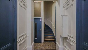 A narrow hallway with a blue door at the end, a patterned floor, and a staircase with a white railing. - Superb AC Apartment Center of Paris (Paris)