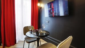 A dining area with a table set for two, a television mounted on the wall, and red curtains.