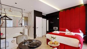 A modern hotel room with a bed, a dining table, and a mirror.