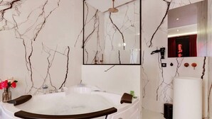 A modern bathroom with a marble wall, a large bathtub, a mirror, and a vanity with a sink.