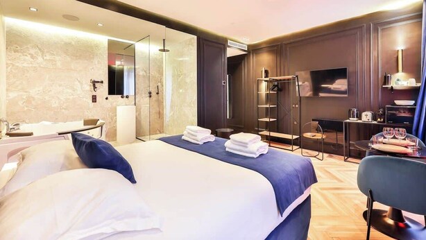 A modern hotel room with a large bed, a separate bathroom, a seating area, and a TV.